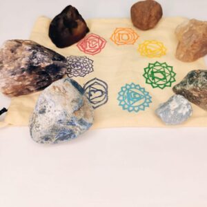 Ensemble de 7 pierres brutes de lithothérapie disposées autour d'un sachet beige imprimé des symboles colorés des chakras