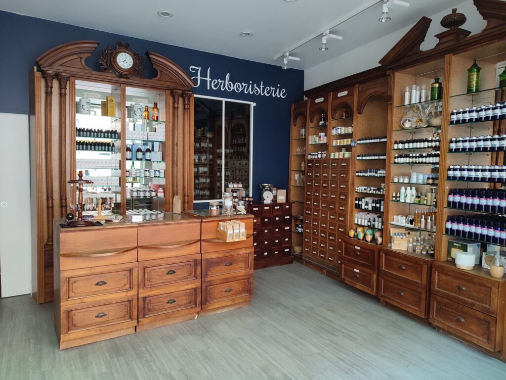 Intérieur d'herboristerie traditionnelle avec de grands meubles en bois, des bocaux et des étagères remplies de flacons, sous un éclairage clair.